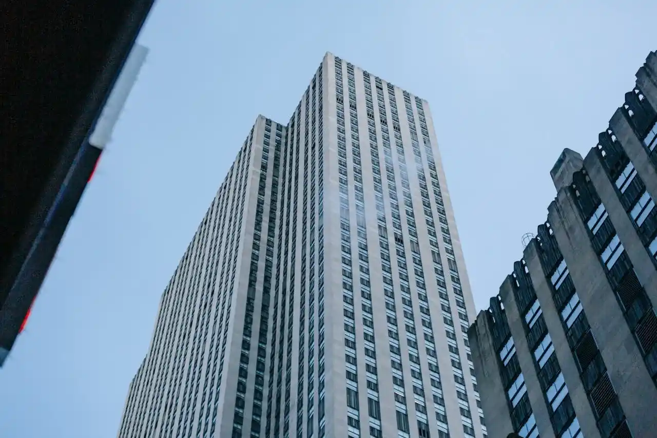 Institutional Excellence - A low-angle shot of a modern glass skyscraper with reflective windows against a clear sky, capturing the corporate power and institutional presence